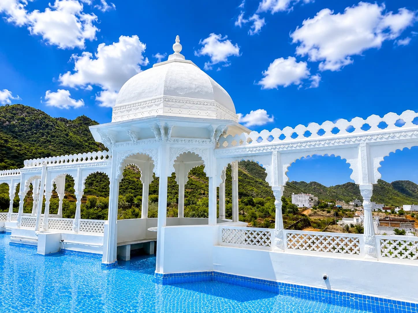 The rooftop pool at MIJMAAN, its white domed chhatri pavilion overlooking the green Aravalli Hills