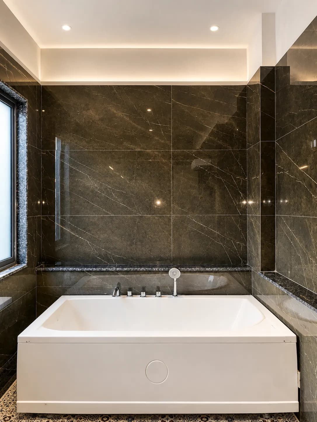 White soaking tub set against dark marble with warm cove lighting