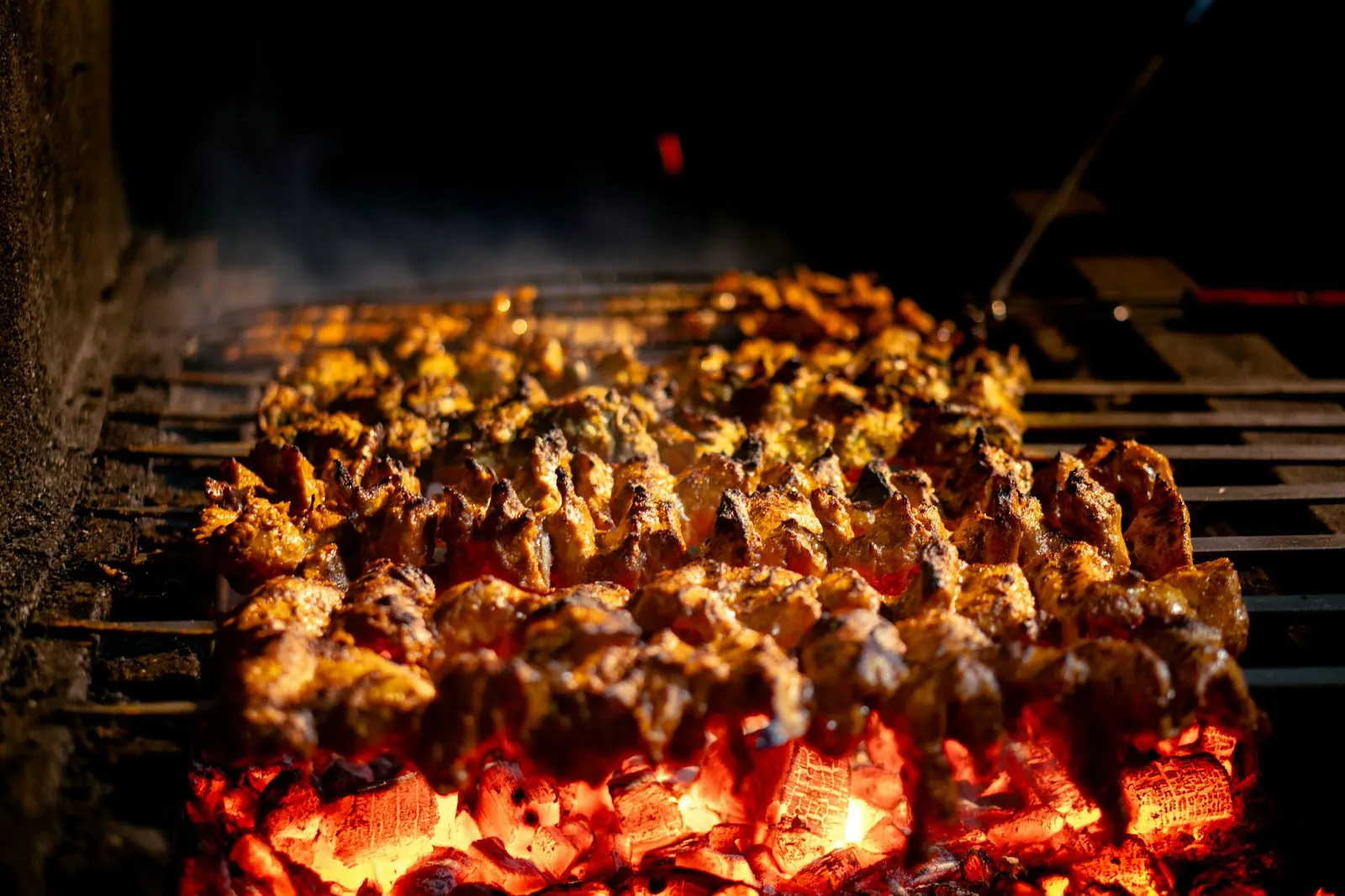 Kebab skewers roasting over glowing coals, smoke rising into the dark