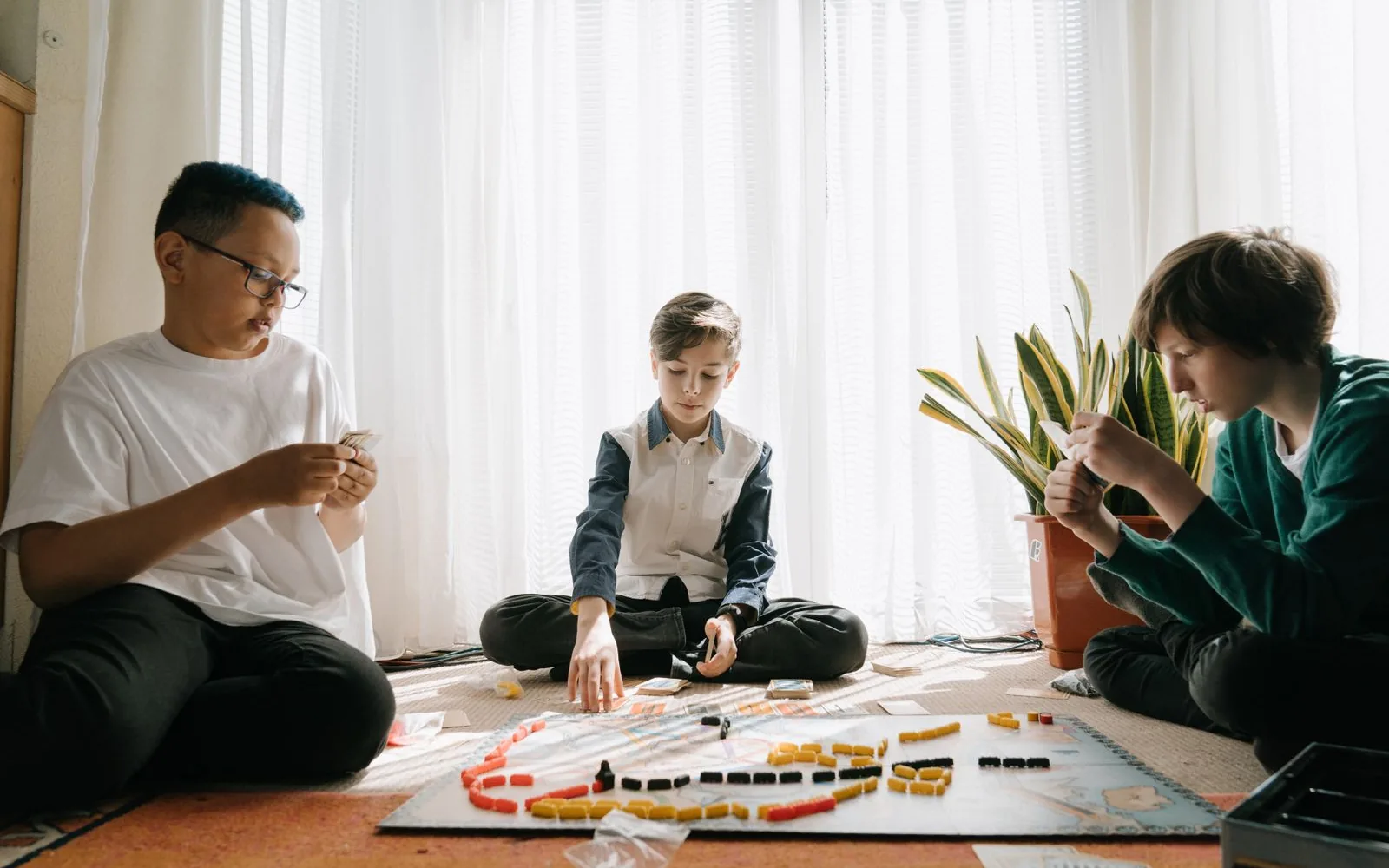 Three children sitting on the floor in soft window light, absorbed in a board game