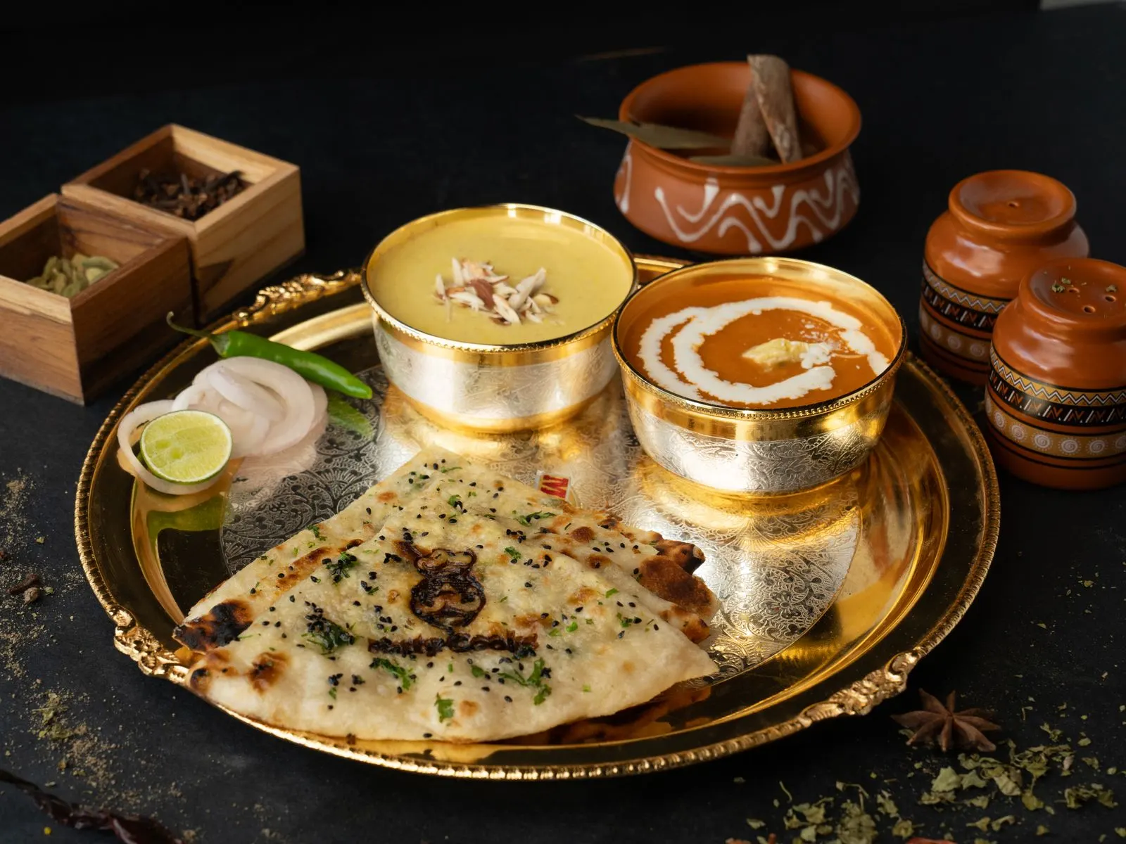 A royal thali on a golden platter — engraved katoris of dal and curry with fresh naan