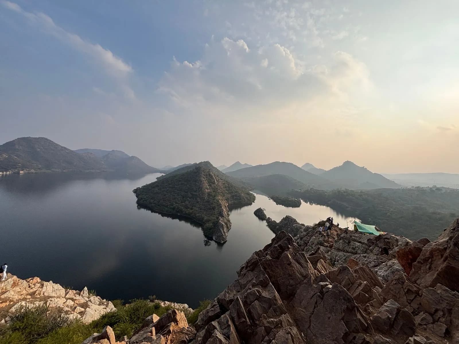 Badi Lake and its island seen from the rocky Bahubali Hills viewpoint at golden hour, framed by the Aravalli hills