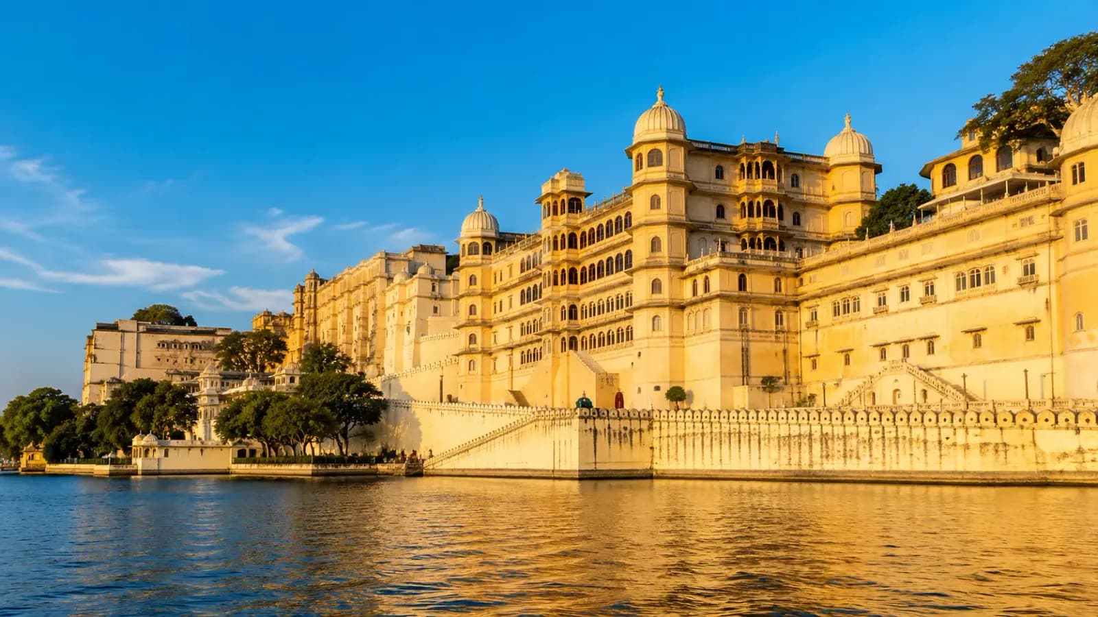 The golden stone towers and domed turrets of Udaipur's City Palace against a blue sky
