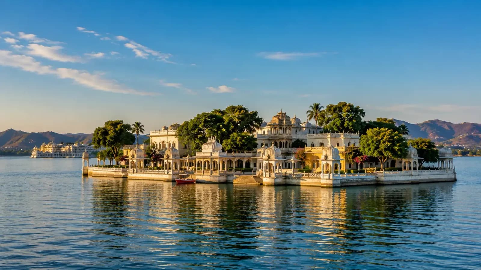 The City Palace glowing across Lake Pichola at sunset in Udaipur, a traditional boat on the water