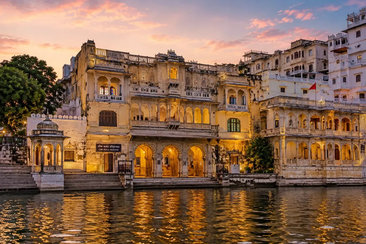 A lit heritage building reflected in Lake Pichola under a pink twilight sky