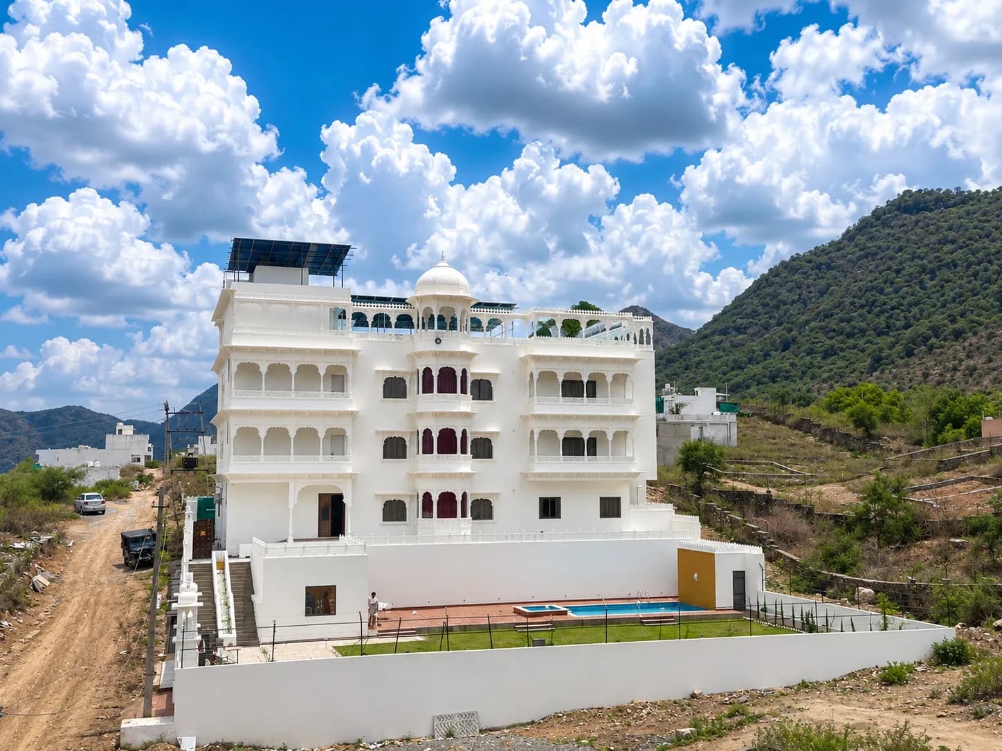 The villa's full white elevation with central dome, jharokha balconies, pool and lawn